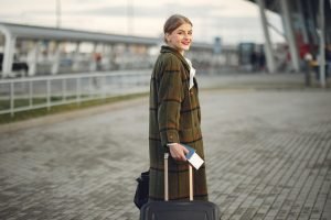 Smiling female walking with a suitcase and a passport near a train station