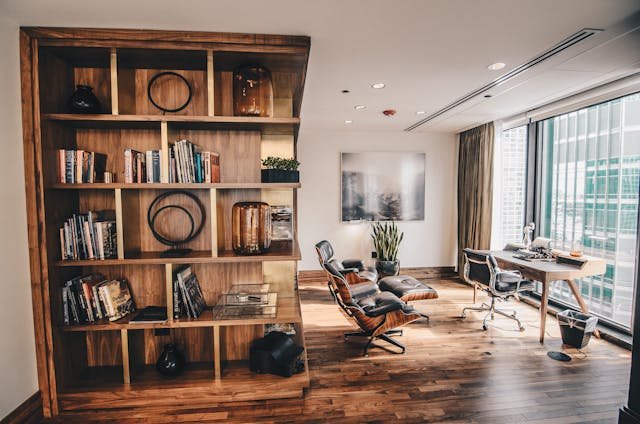 A modern and spacious home office after moving to Rockville, featuring a wooden bookshelf filled with books, an ergonomic chair, a desk, and a large window