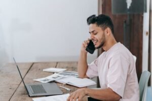 Man negotiating over the phone with a moving company while sitting at a desk.