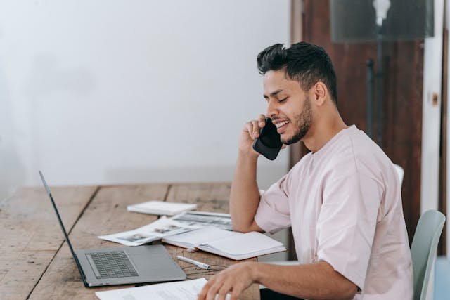 Man negotiating over the phone with a moving company while sitting at a desk.