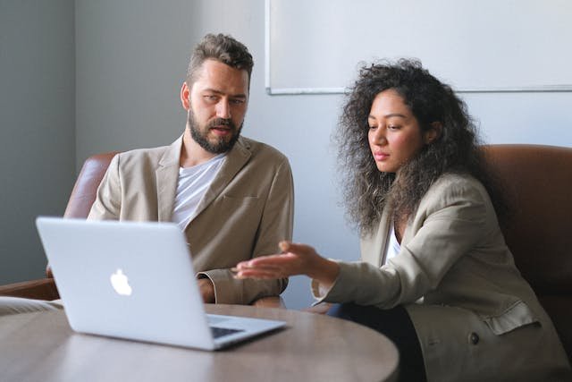Two professionals reviewing a laptop screen with documents in an office setting.