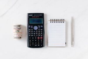 A calculator, notepad, pen, and cash money on a white surface