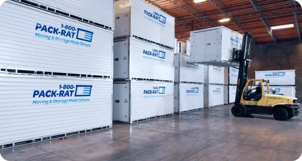 Stacked 1-800-PACK-RAT moving containers inside a PACK-RAT storage warehouse with a forklift